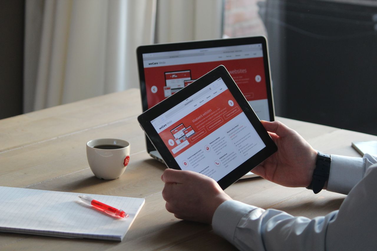 services-03 Business professional using a tablet and laptop with a hot drink, focusing on digital content review.